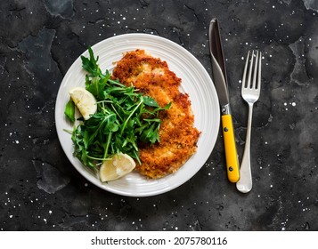 Garlicky bread crumbs crispy turkey schnitzel and fresh lemon arugula salad on a dark background, top view - Shutterstock ID 2075780116