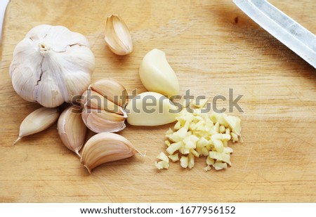 Garlics and garlic chopped with knife on right side 
 on light wooden path background