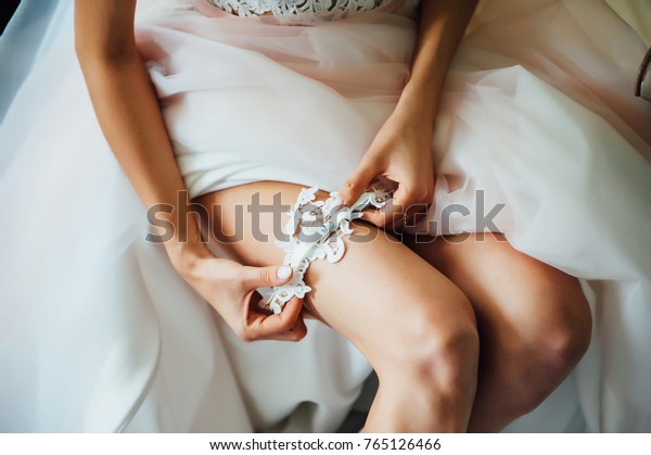 Garter on the leg of a bride, slim sexy bride in\
wedding luxury dress showing her silk garter with golden ribbon.\
woman have a final preparation for wedding ceremony. Wedding day\
moments