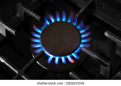 Gas burner with a blue flame on a black kitchen stove, with a cast-iron grate, top view, selective soft focus. gas crisis.
