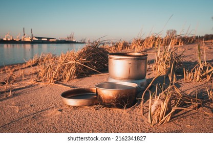 Gas cooker with aluminium pot and plate at Harriersand beach next to Weser river during golden hour.