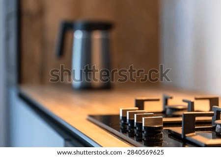 Gas cooktop knobs on kitchen counter. Electric kettle blurred in modern interior.