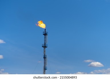 A gas flare at a field in the Perm region (Russia) against a blue sky. Gas tower with a bright pillar of fire. Flaring of associated petroleum gas. Photo minimalism.