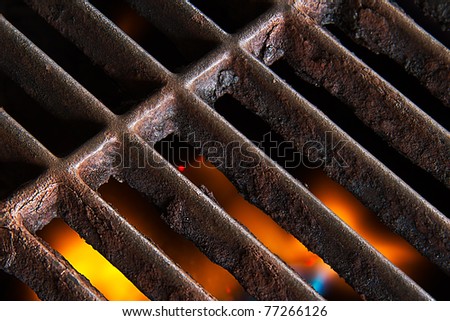 A gas grill with open flames below the rusty iron grate.