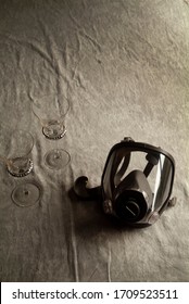 A Gas Mask And Two Wine Glasses Rest Side By Side On A Dining Room Table.