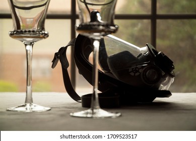 A Gas Mask And Two Wine Glasses Rest Side By Side On A Dining Room Table.