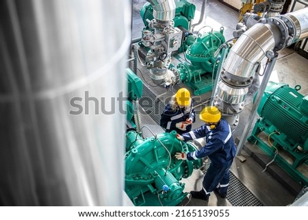 Gas and oil industrial workers working together and checking pipeline and engine pumps in factory.