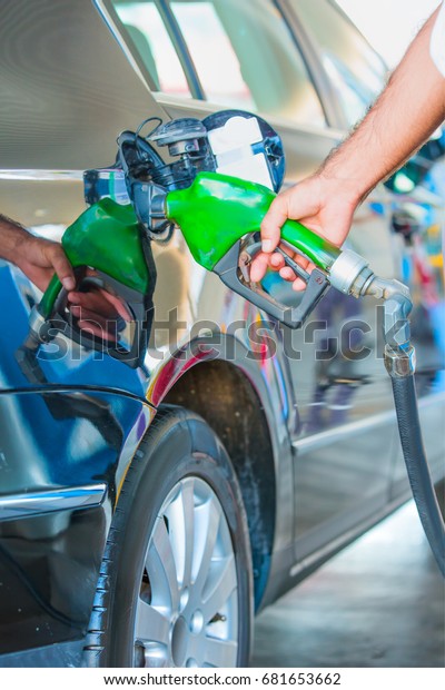 Gas pump\
nozzle in the fuel tank of a black\
car.