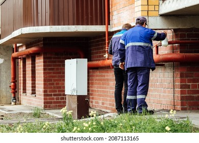 The Gas Service Repairs The Pipe In The House. Workers In Blue Uniforms Check The Condition Of Communications In The Building. Pipeline Repair And Maintenance