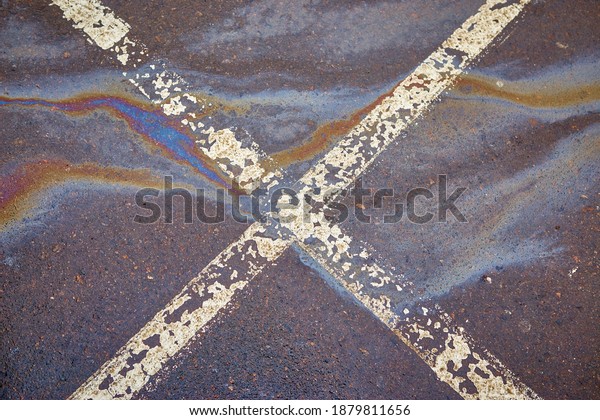 Gas stain on wet asphalt in\
the car park caused by a leak under a car or truck, abstract\
background