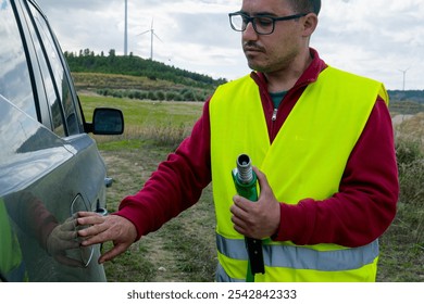 Gas station attendant is getting ready to refuel a car in a rural area, with wind turbines in the background, suggesting sustainable practices - Powered by Shutterstock