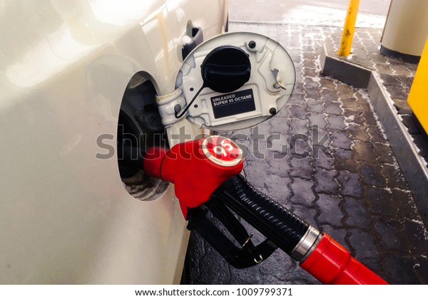 At the gas\
station, the gun is filled with gasoline into the hatch of the car.\
The city is bright in the\
afternoon.