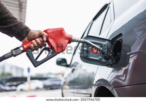 A gas station worker holds\
a fuel dispenser to fill the car with fuel. A young man\'s hand\
holds a gas nozzle to refuel with self-service in a gas\
station.