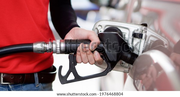 Gas station\
worker in red uniform filling up bronze pickup truck tank. Closeup\
hand holding black gas pump\
nozzle.