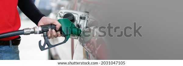 Gas station\
worker in red uniform filling up bronze pickup truck tank. Closeup\
hand holding green gas pump\
nozzle.