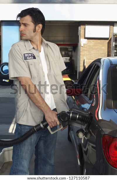 Gas station worker refueling the car\
tank while looking over shoulder at petrol\
station