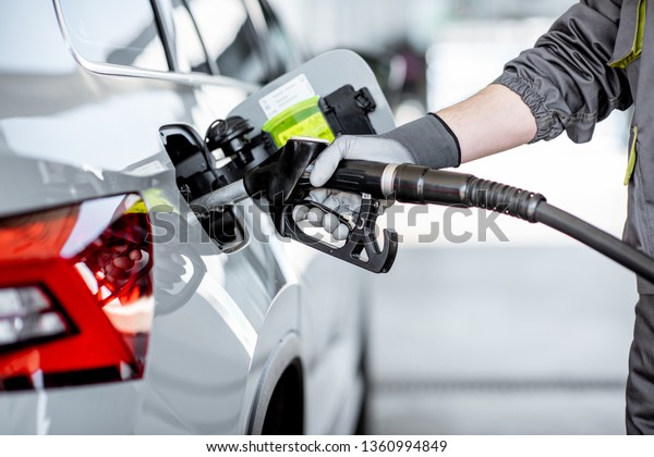 Gas station worker refueling car with\
gasoline, close-up view focused on the filling\
gun