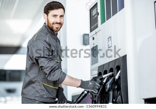 Gas station worker in uniform taking filling\
gun, refueling car at the gas\
station