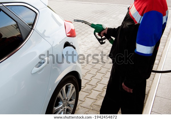 Gas station worker in\
workwear refueling luxury car with gasoline holding filling gun at\
the station.