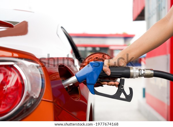 Gas station worker\'s hand\
holding blue benzene gas pump, filling up red sport car tank. Close\
up