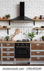 Gas stove, built in oven equipment, cooking hood, kitchenware supplies, green houseplant decor and new furniture against brick wall. Vertical view of wooden kitchen facade in modern interior house