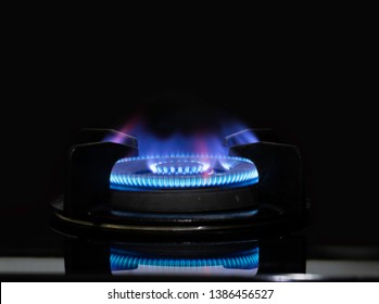 Gas stove burner with blue flames and dark background.