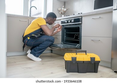 Gas Stove Repair. Dark-skinned Service Man In Yellow Tshirt Repairing The Gas Stove