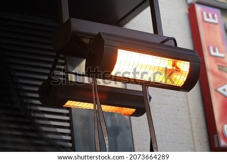 Gas terrace heater or radiant heater under the high roof of a public café. Inefficient and climate-damaging waste of heating energy, climate killer.