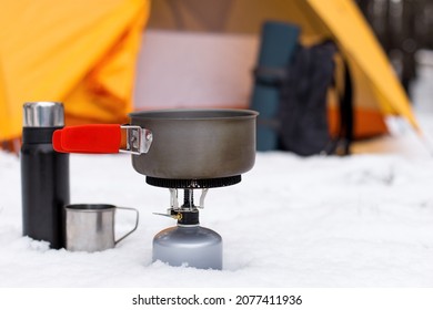 Gas tourist burner and pot, against the background of tent. Equipment for winter hiking, tourist cuisine.