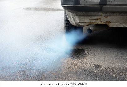 Gases emitted from the exhaust pipe dark old car, standing on the pavement.