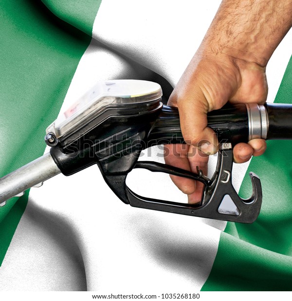 Gasoline consumption concept - Hand holding hose\
against flag of\
Nigeria