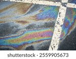 Gasoline or oil spill creating rainbow sheen on asphalt parking lot surface.