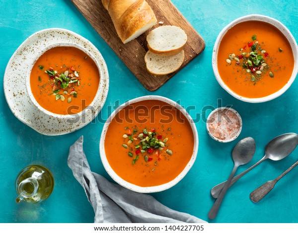 Gaspacho soup on blue tabletop. Three bowls of\
traditional spanish cold soup puree gaspacho or gazpacho on bright\
blue background. Top view or flat\
lay.