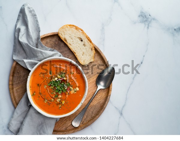 Gaspacho soup on round wooden tray over white marble
tabletop. Bowl of traditional spanish cold soup puree gazpacho on
light marble background. Copy space for text or design. Top view or
flat lay.