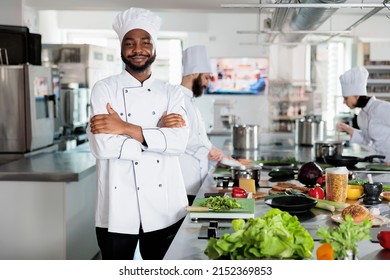 Gastronomy expert standing in restaurant professional kitchen with arms crossed while smiling at camera. Confident head chef wearing cooking uniform while preparing ingredients for dinner service. - Shutterstock ID 2152369853