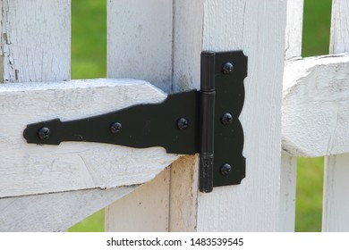 Gate Hinge On A White Picket Fence. Close Up Of Black Iron Hinge.