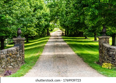 Gated open entrance with road driveway in rural countryside in Virginia estate with stone fence and gravel dirt path street with green lush trees in summer