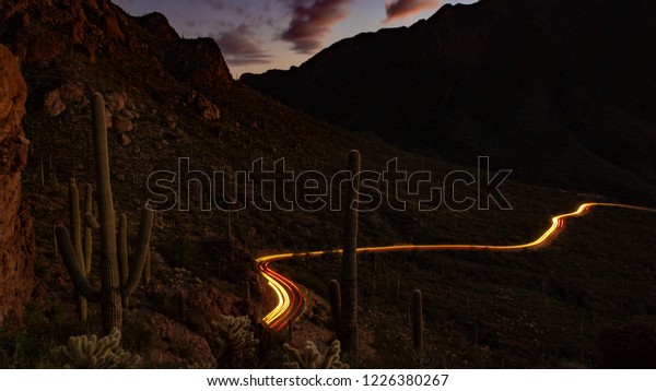 Gates Pass in\
Saguaro National Park west of Tucson, Arizona. Light Trails from\
passing cars and cactus covered mountains, beautiful clouds at\
sunset looking down on a scenic road.\
