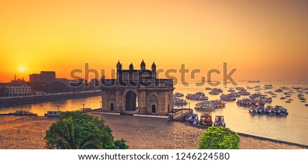 The gateway of India at sunrise with beautiful reflections in the sea. Boats in the water in a hot day.