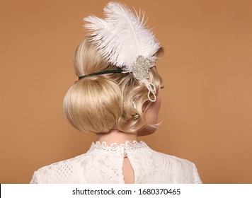 Gatsby Style. Portrait Of Retro Woman With Shiny Wavy Hairstyle, Feather In Head. Back View Of Elegant Lady Posing Isolated On Studio Beige Background. Beautiful Blonde Bride. 