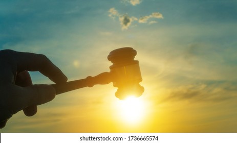 Gavel in the hand of a judge on sunset sky background. Verdict, court, crime and punishment - Powered by Shutterstock