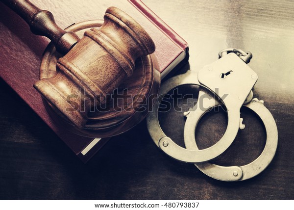 Gavel\
and handcuffs with red legal book on wooden\
table