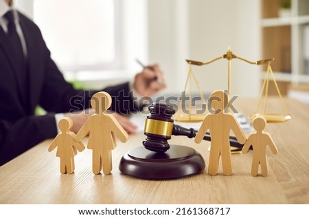 Gavel, sound block and little wooden figures of parents and children placed on desk in courthouse up close, judge and scales of justice in background. Family law, court, divorce, child custody concept