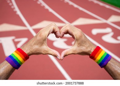 Gay Athlete Wearing Rainbow Pride Wristbands Making Love Heart Hands Gesture Against A Red Athletic Track Background