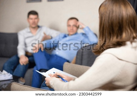 Gay clients answers questions from specialist at psychologist appointment. Woman listens to answers and makes notes of important points