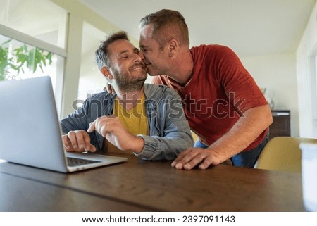 Gay couple celebrates and kisses while organizing their Valentine's trip in front of the laptop