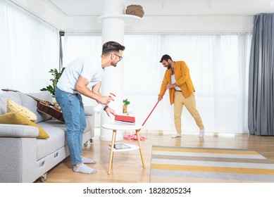 Gay Couple Cleaning Living Room With Mop And Spray Bottle 