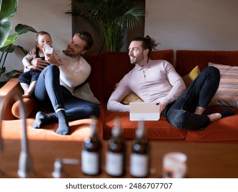 Gay couple feeding baby daughter on sofa at home - Powered by Shutterstock