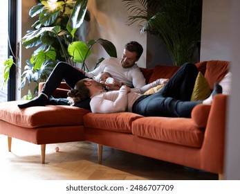 Gay couple feeding baby daughter on sofa at home - Powered by Shutterstock