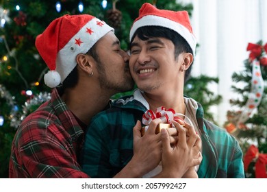 Gay couple kissing on Christmas day at home and holding Christmas gift, in front of Christmas tree, LGBTQ concept - Powered by Shutterstock